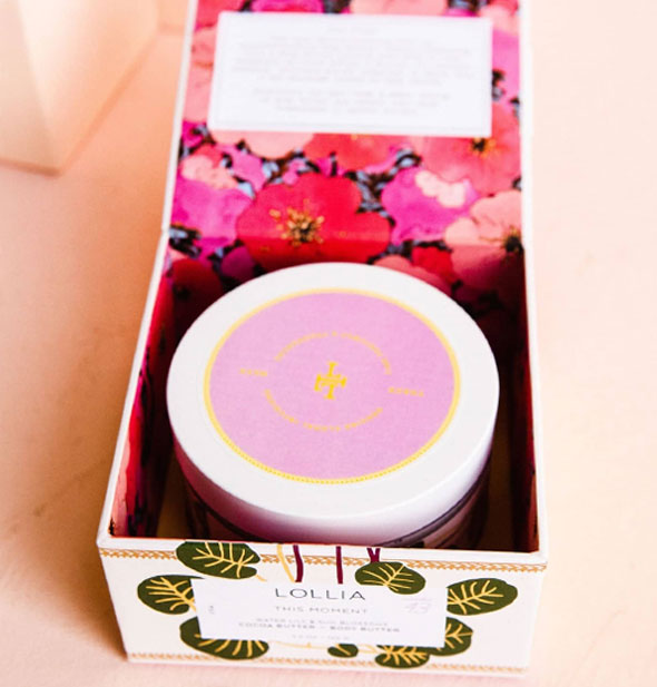 Opened box of Lollia This Moment Body Butter shows brightly colored floral lining and a jar of body butter inside with purple label on the lid