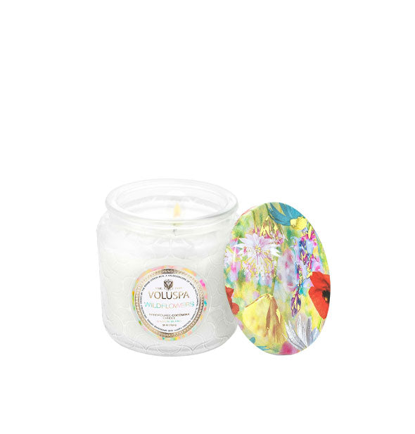 White glass jar Voluspa candle with colorful floral lid set to the side