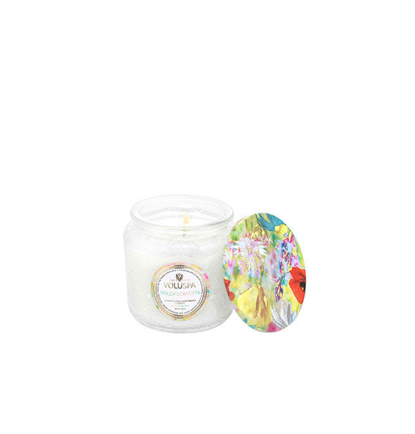 White glass jar Voluspa candle with colorful floral lid set to the side