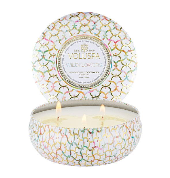 White Wildflowers Voluspa candle tin with three lit wicks inside and a colorful lattice pattern with gold accents