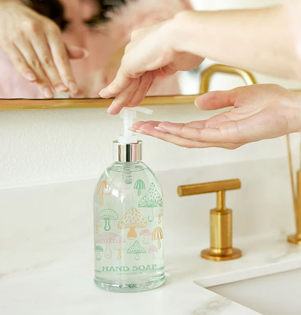 Model dispenses liquid hand soap from a mushroom-patterned bottle on a bathroom countertop