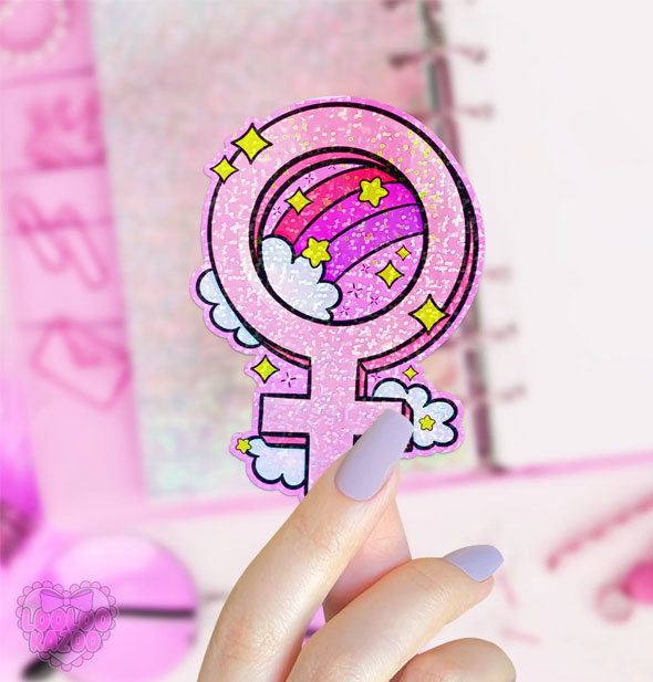 Model's hand holds a pink sparkly female symbol sticker accented with a rainbow and clouds and yellow stars