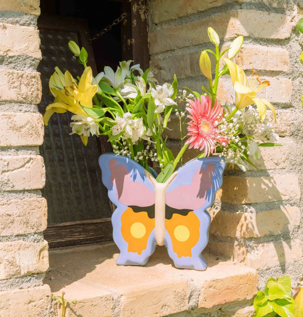 Butterfly vase resting on a brick windowsill holds a bouquet of fresh flowers