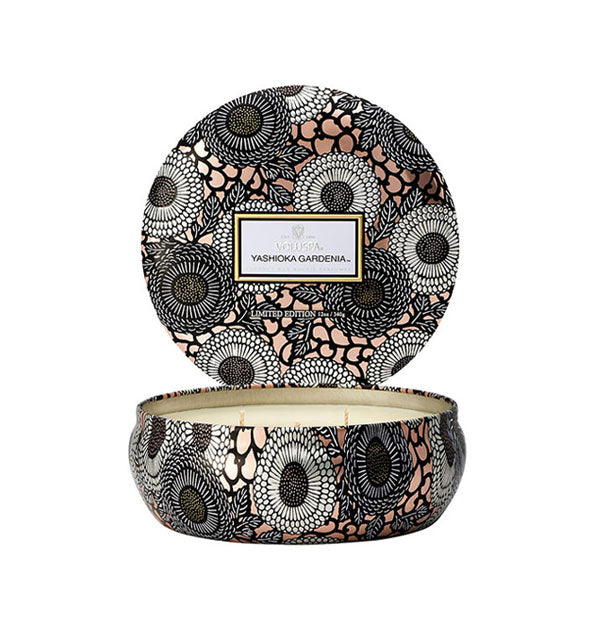 Round black, silver, and rose gold Voluspa Yashioka Gardenia candle tin with lid removed and set upright behind the tin