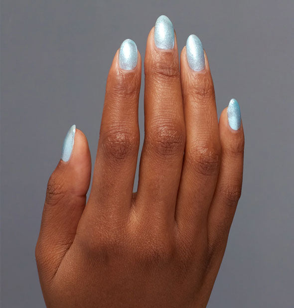 Model's hand wears a light, iridescent, shimmery shade of blue nail polish