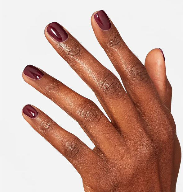 Model's hand wears a dark purplish-red shade of nail polish