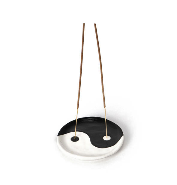Round black and white incense dish holds two incense sticks, each emerging from a hole in the center of each dot in the design