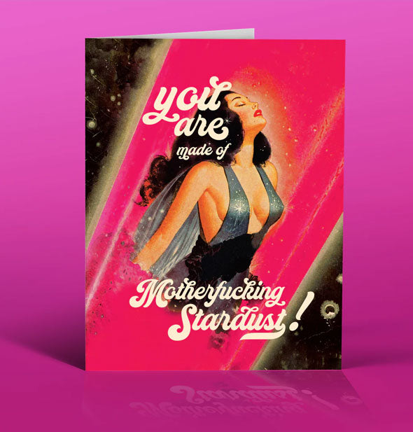 Greeting card on purple backdrop says, "You are made of Motherfucking Stardust!" in white script surrounding an image of a woman with eyes closed wearing a low-cut silver sparkly outfit