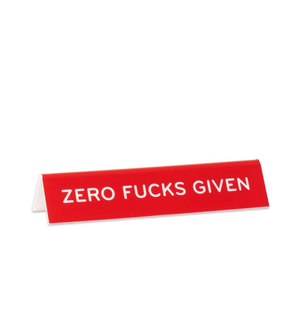 Rectangular red desk sign says, "Zero fucks given" in white lettering