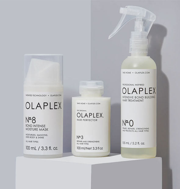 Bottles of Olaplex No. 8 Bond Intense Moisture Mask, No. 3 Hair Perfector, and No. 0 Intensive Bond Building Hair Treatment on a square platform