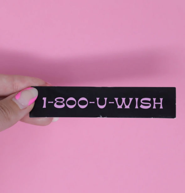 Model's hand holds a rectangular black sticker that says, "1-800-U-WISH" in pink lettering