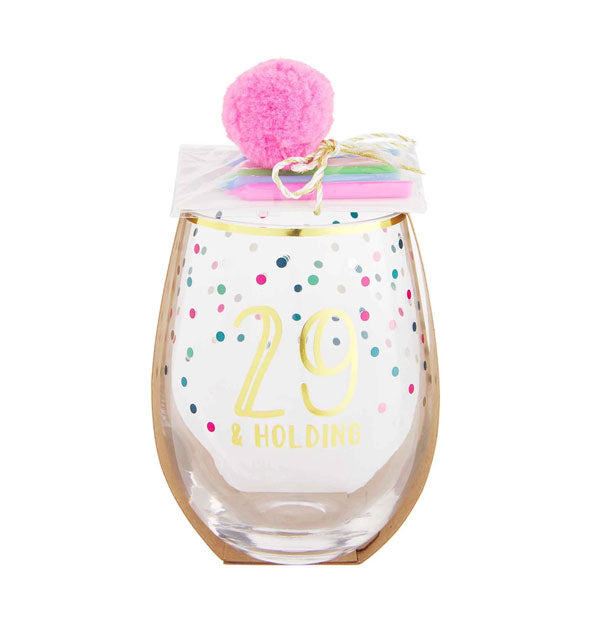 Stemless wine glass with gold rim, colorful confetti design, and pink pom pom with birthday candle pack attached says, "29 & Holding" in gold foil lettering