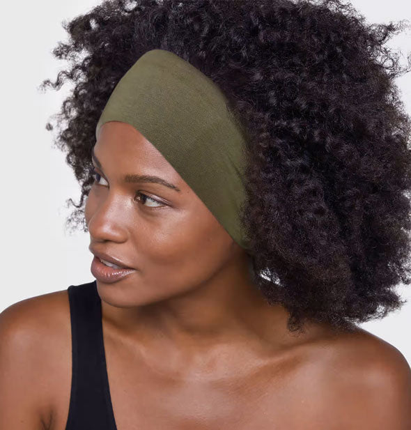Model with head turns to the side wears a wide olive green cloth headband at the front of hair