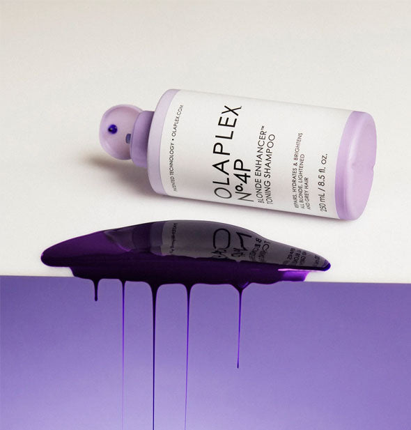 An overturned bottle of 8.5 ounce bottle of Olaplex No. 4P Blonde Enhancer Toning Shampoo sits next to a purple puddle of product dripping over the surface's edge