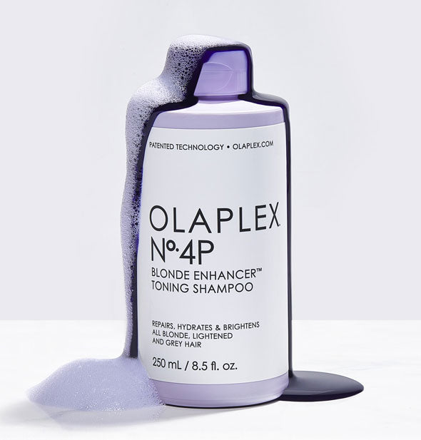 A bottle of Olaplex No. 4P Blonde Enhancer Toning Shampoo is coated with its sudsy purple contents