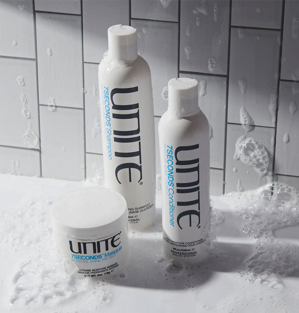 Unite 7SECONDS Shampoo, Conditioner, and Masque on a white tiled backdrop with soapy suds all over