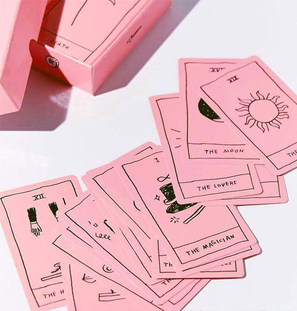 Sample cards from the OK Tarot deck are spread out haphazardly on a white surface near their box packaging