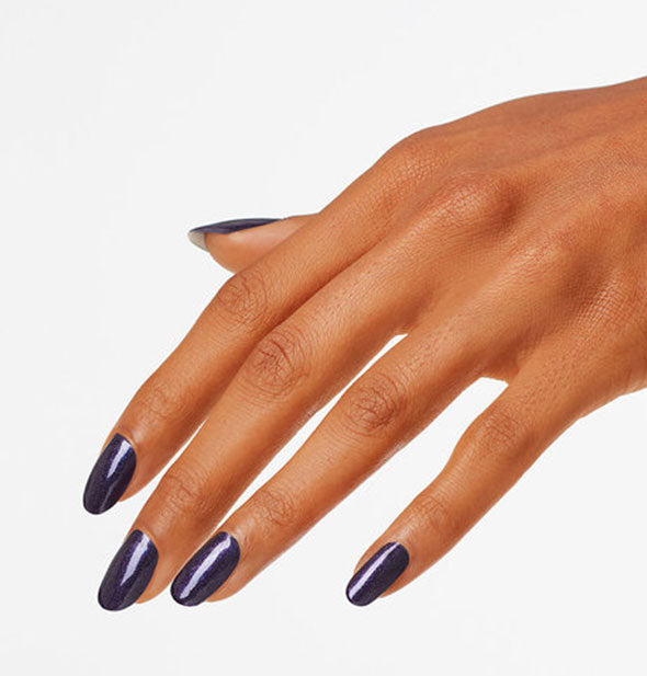 Model's hand wears a dark blueish purple shade of nail polish