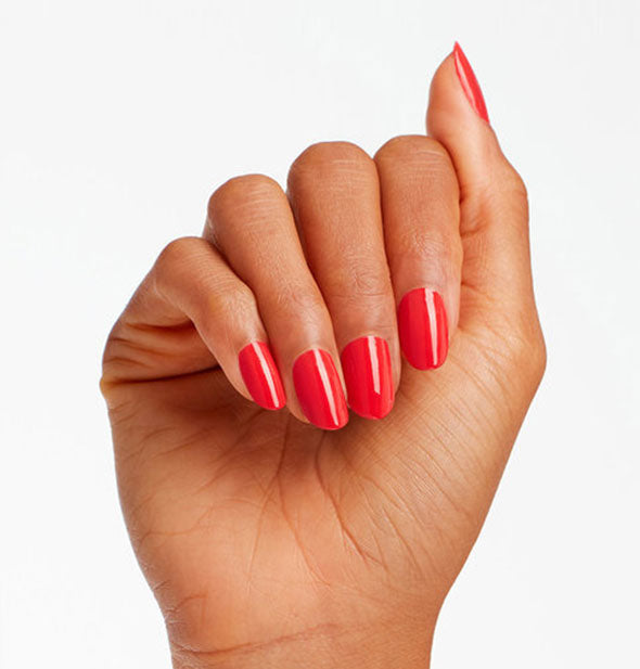 Model's hand wears a hot coral shade of nail polish