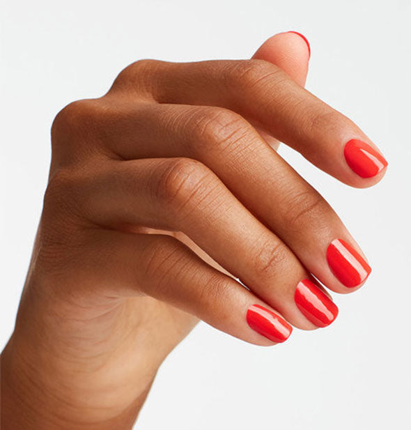 Model's hand wears a bright orange-red shade of nail polish