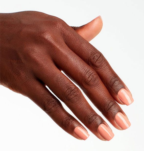Model's hand wears a peachy-pink shade of nail polish