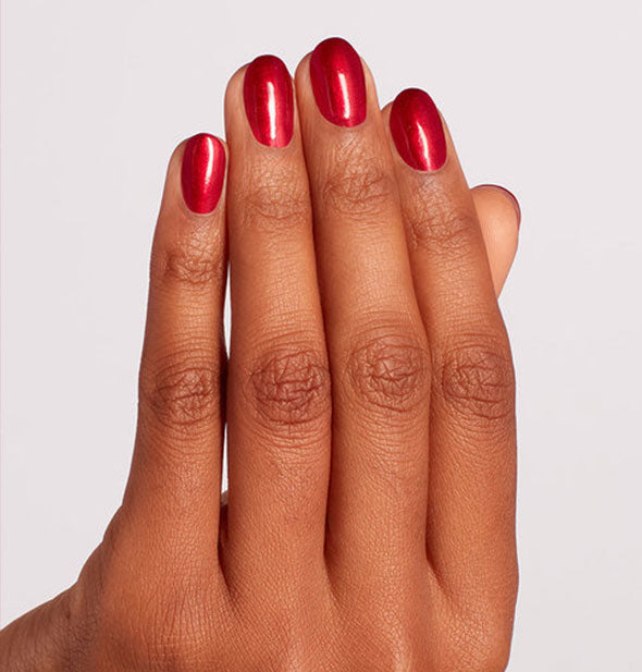 Model's hand wears a shimmery shade of red nail polish