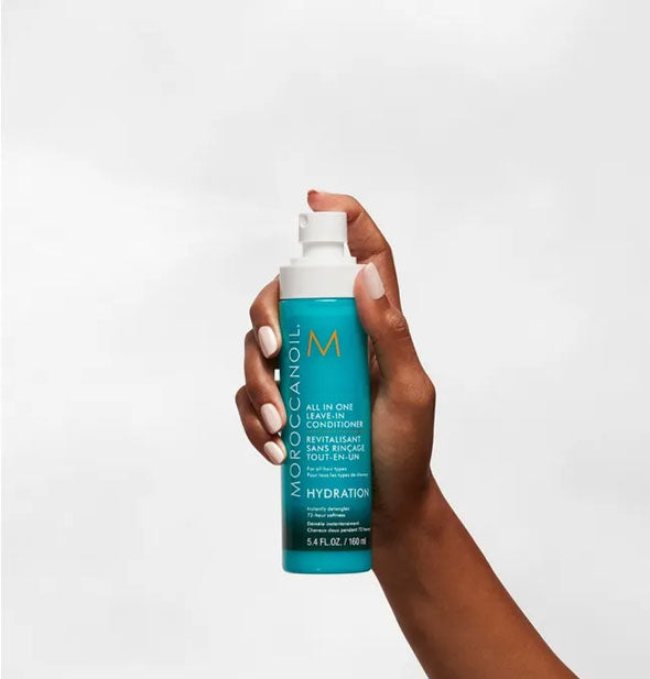 Model's hand dispenses a fine mist of Moroccanoil All In One Leave-In Conditioner spray