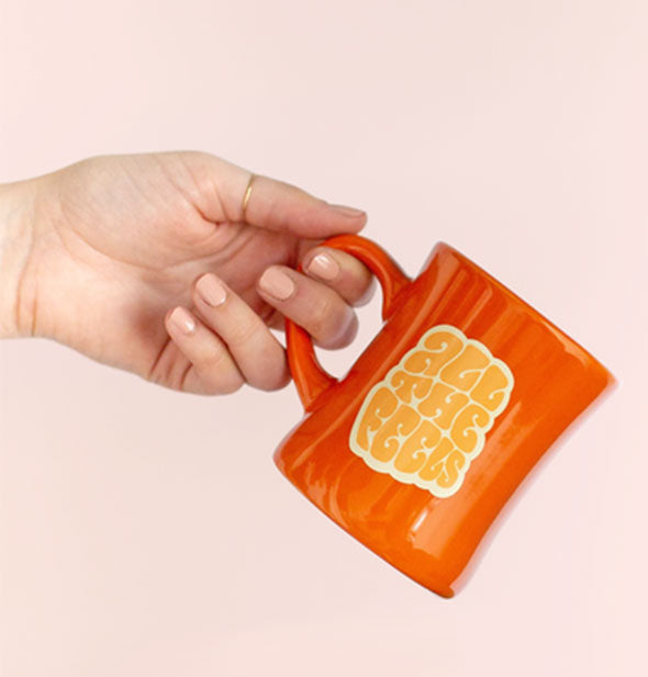 Model's hand holds the orange All the Feels diner-style coffee mug by the handle