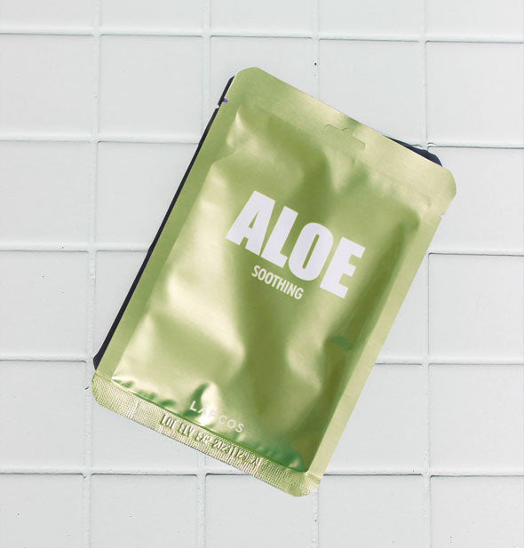 Green foil Aloe Soothing mask packet by Lapcos rests on white tile