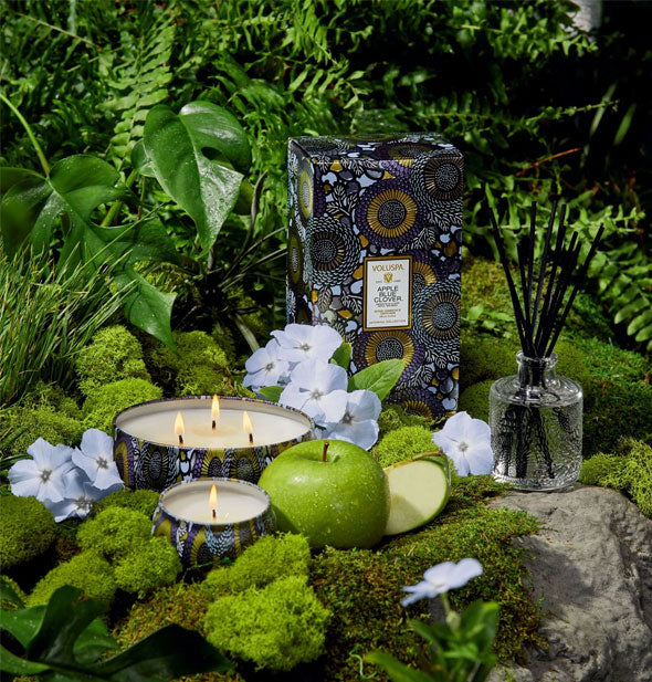 Apple Blue Clover Voluspa candles staged on a mossy surface with botanical backdrop