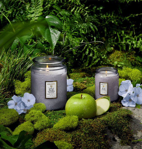 Apple Blue Clover Voluspa candles staged on a mossy surface with botanical backdrop and green apple