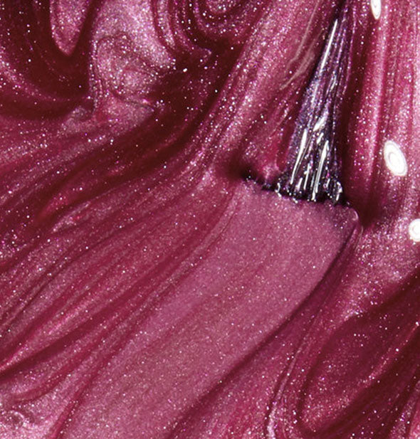 Closeup of shimmery pinkish purple nail polish with brush tip drawn through