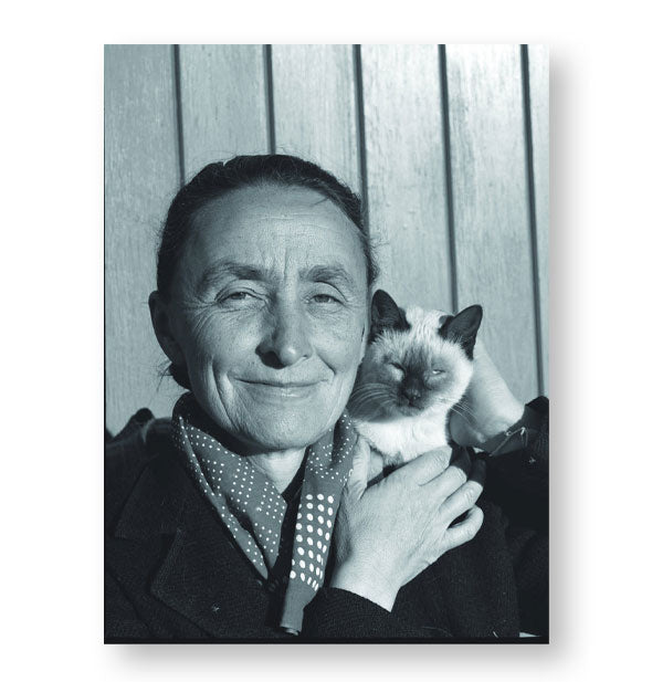 Black and white photograph from Artists and Their Cats features Georgia O'Keeffee holding her Siamese cat against a wooden backdrop