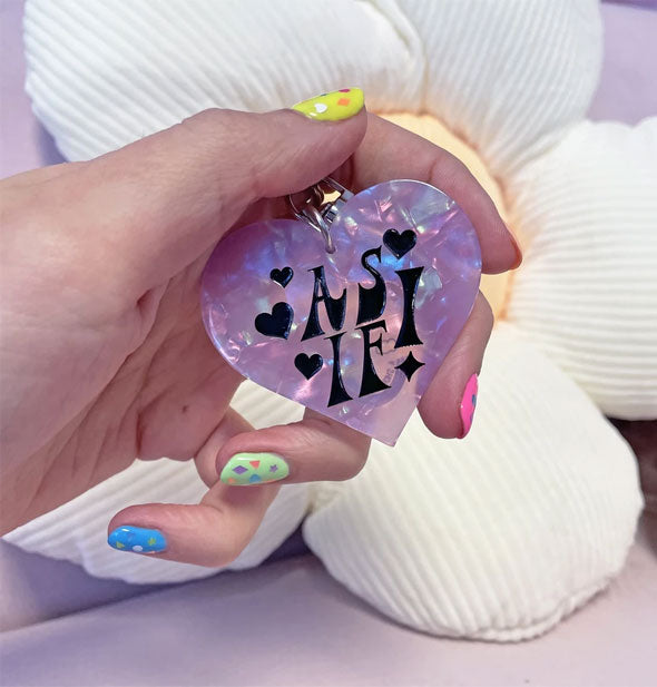 Model's hand holds an As If! purple heart-shaped keychain