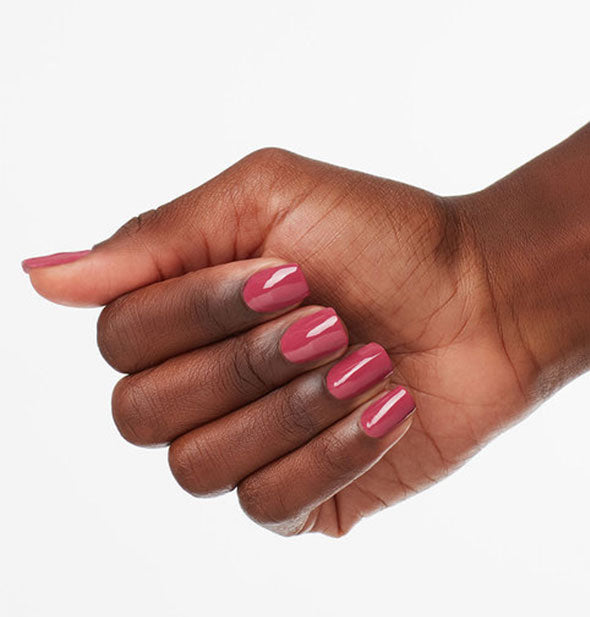 Model's hand wears a dark, dusty shade of pink nail polish
