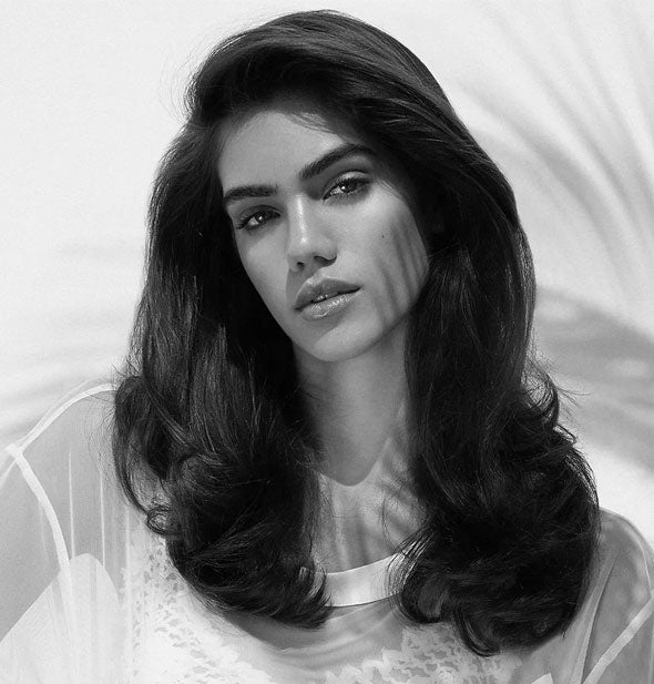 Model wears hair in a long, voluminous style with some curl at the ends