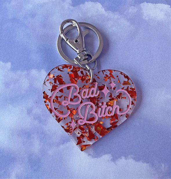 Clear heart-shaped keychain with red foil flecks throughout and the words, "Bad Bitch" in pink script with star accents; silver hardware at top