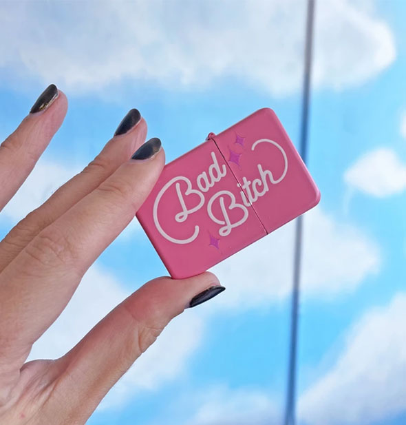 Model's hand holds up the Bad Bitch lighter in front of a cloud print backdrop