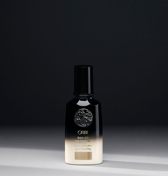 Small black and white bottle of Oribe Balm d'Or Heat Styling Shield on a dark gray background