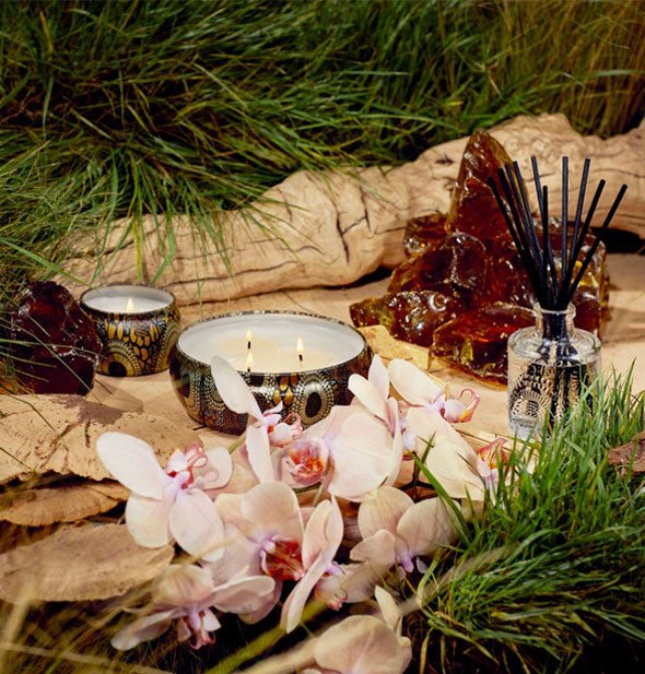 Decorative tin candles are staged with amber quartz and pink orchids against a grassy backdrop with tree branch