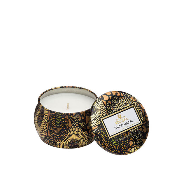 A small unlit candle inside a rounded tin with metallic floral design and matching lid set to the side.