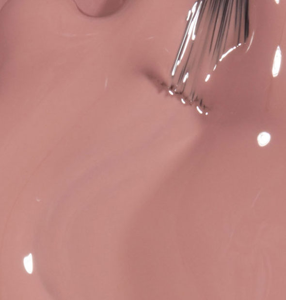 Closeup of beige-pink nail polish with brush tip drawn through it