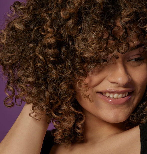 Model fluffs curls that have been styled with Bumble and bumble Curl Anti-Humidity Gel-Oil