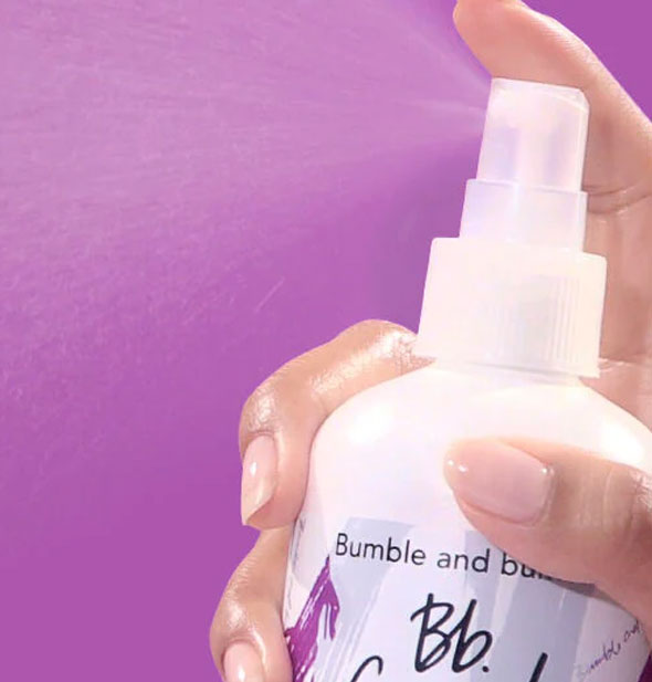 Model's hand dispenses a fine mist from a Bumble and bumble Curl Reactivator bottle to show product consistency