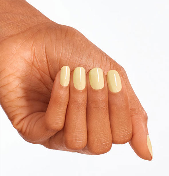 Model's hand wears a muted pastel yellow shade of nail polish