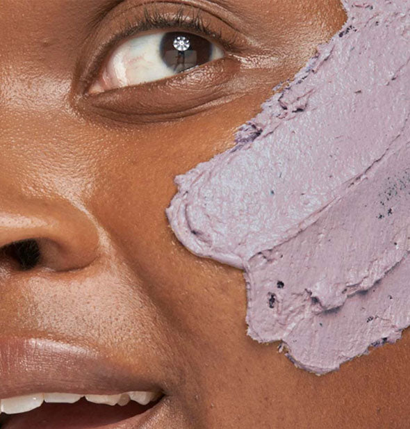 Closeup of model's cheek shows applied streaks of a purple face mask