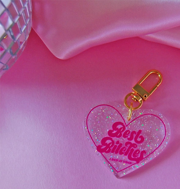 Clear glitter heart-shaped keychain with gold clasp hardware says, "Best Bitches" in pink lettering in a pink heart-shaped border