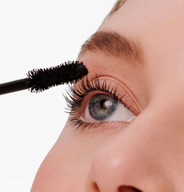 Model applies mascara to lashes with applicator wand