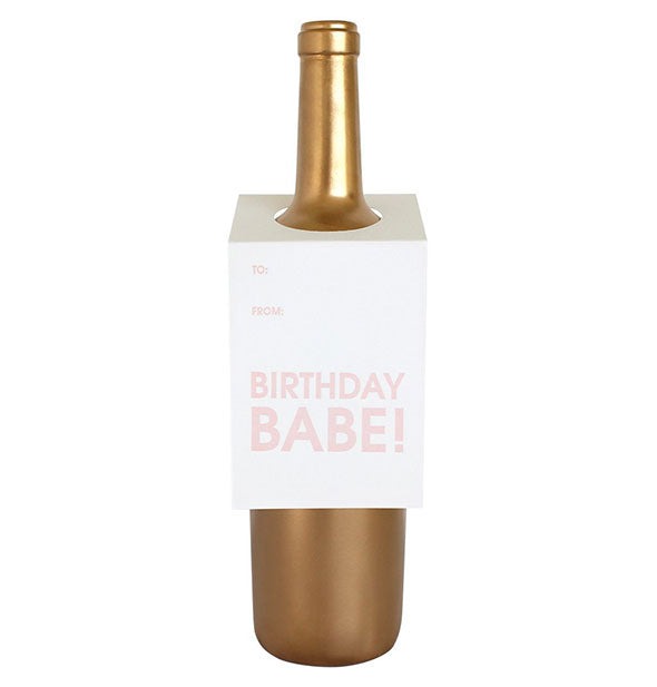 White card that says, "Birthday babe!" in light pink lettering hangs on the shoulder of a gold wine bottle