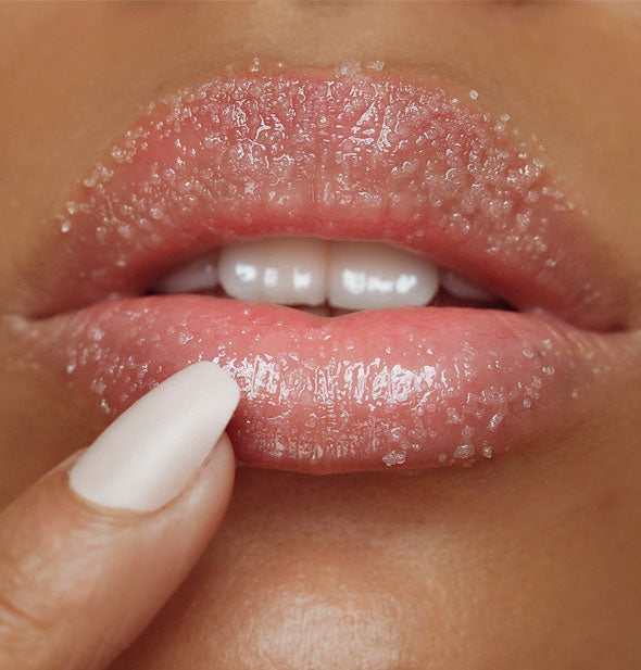 Model applies sugar scrub to lips with fingertip